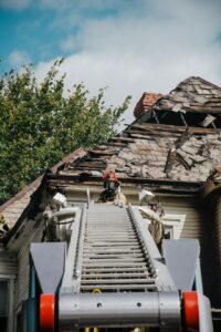 Homeowner inspecting roof shingles and gutters from the ground beside a ladder and maintenance checklist.