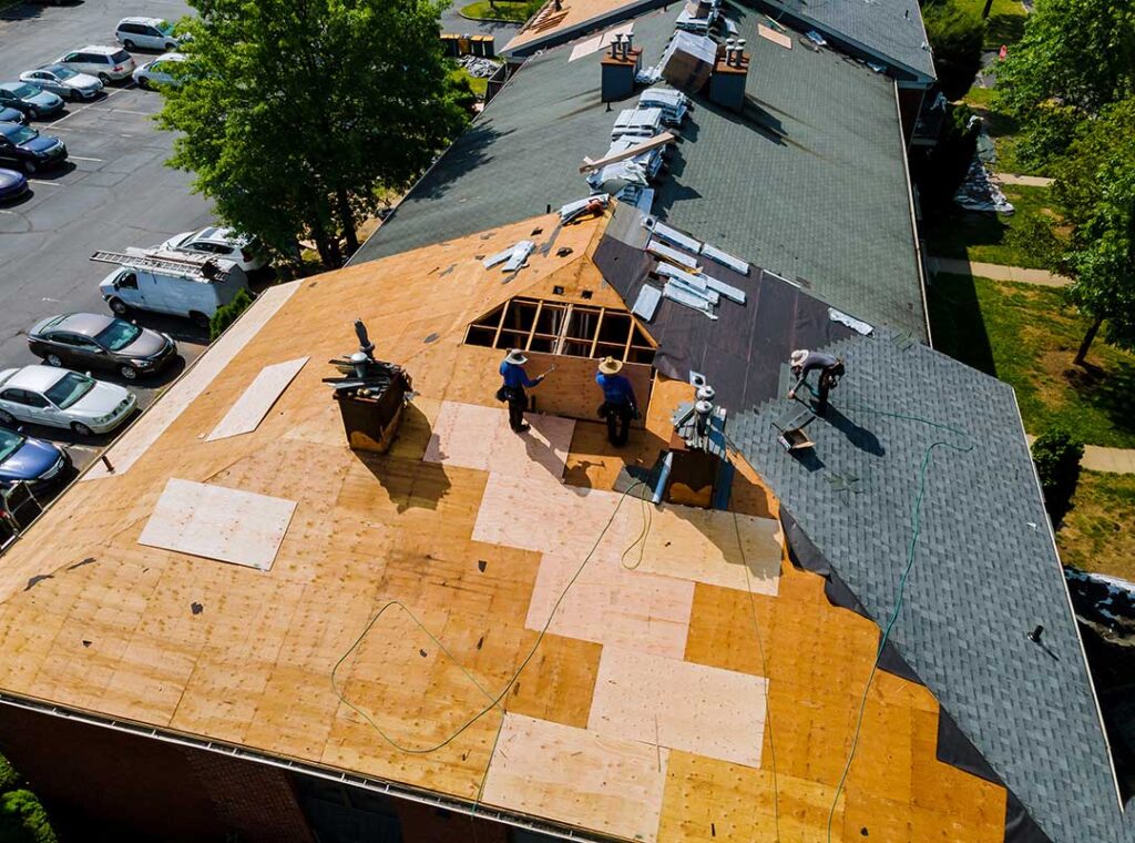 Roofing worker examines shingles and flashing with a moisture meter on a snow-dusted residential roof.